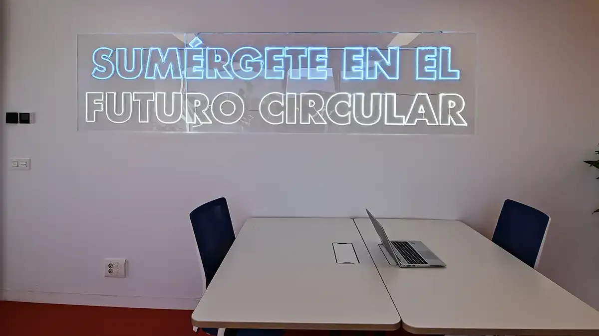 Mesas y sillas baja un letraro de neón con el lema "Sumérgete en el futuro circular".