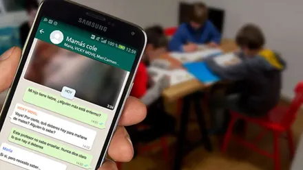Mano sosteniendo un móvil con un mensaje de whatsapp de las madres del colegio.