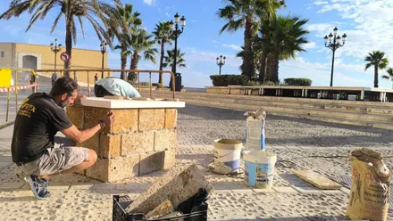 El escultor Manuel Jesús Sánchez Parra, de espaldas, prepara con herramientas la base de hormigón sobre la que se instalará la estatua de Juanito Villar, en la plaza Canal de Ponce.