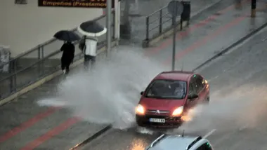 Un coche salpica a dos viandantes al pasar por un carcho formado en la Avenida de la Sanidad Pública de Cádiz en octure de 2024.