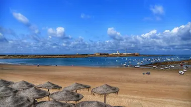 Playa de la Caleta con bajamar y cielo azul. Al fondo, el Castillo de San Sebastián