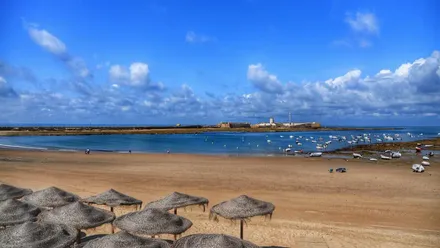 Playa de la Caleta con bajamar y cielo azul. Al fondo, el Castillo de San Sebastián
