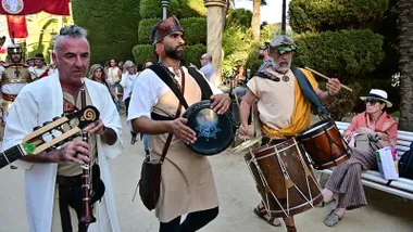 Grupo de músicos con diferentes instrumentos y vestidos de época tocando mientras desfilan entre el público.