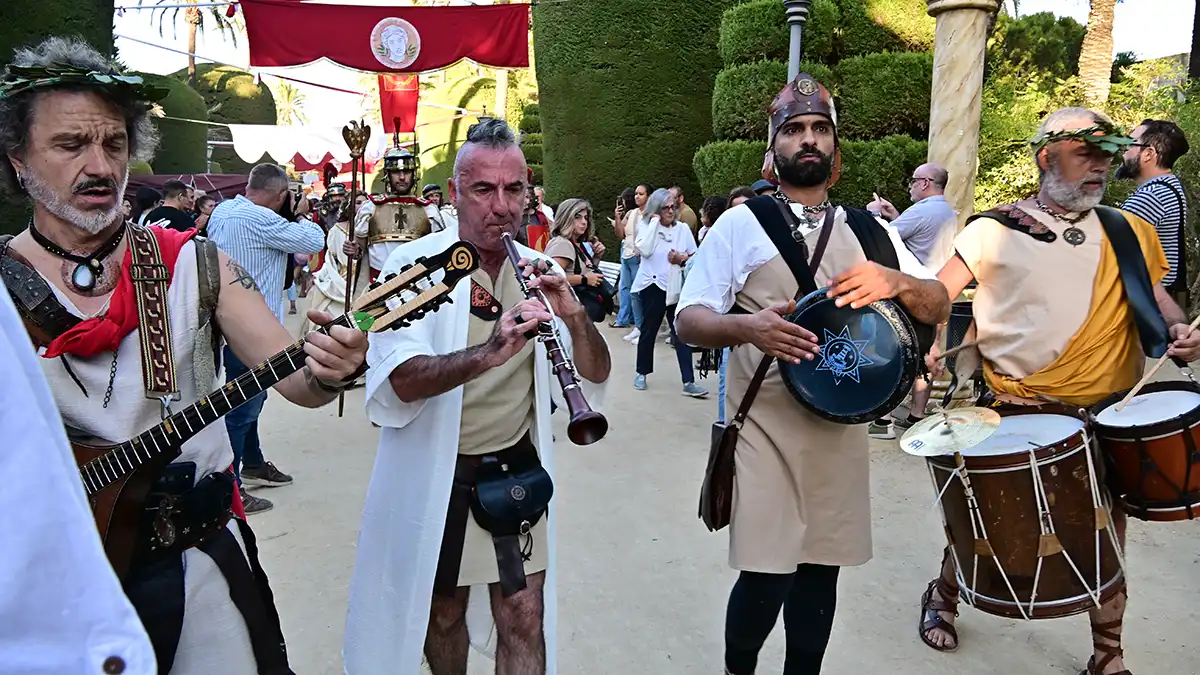 Grupo de músicos con diferentes instrumentos y vestidos de época tocando mientras desfilan entre el público.