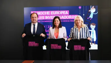 Patricia Cavada y los organizadores sosteniendo una camiseta negra con letras rosas de "La Noche de los Investigadores".