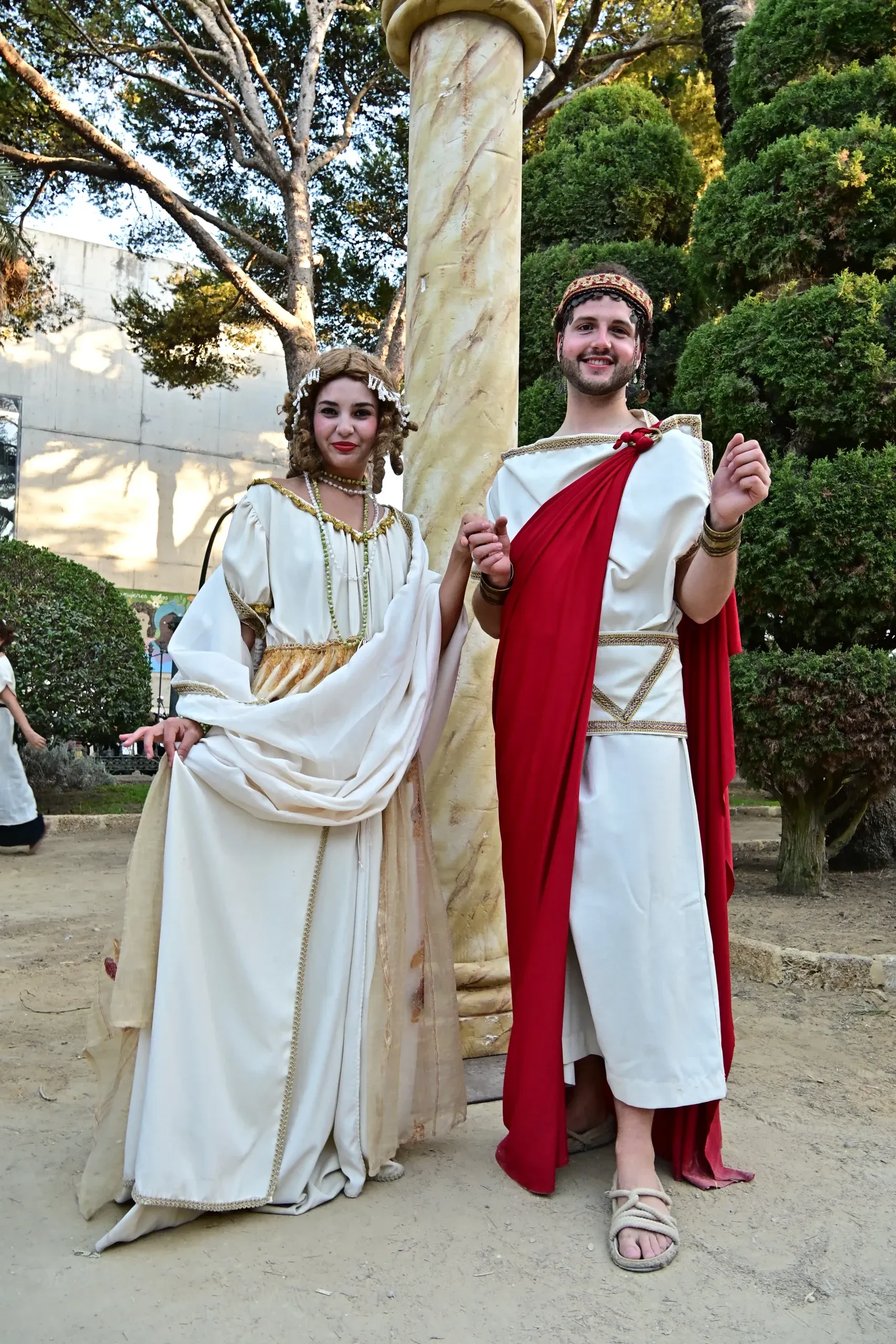 Pareja vestida con túnicas romanas posa ante una columna sonriendo.