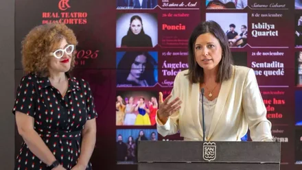 Patricia Cavada, con chaqueta clara, y la concejala de cultura, tras ellas el panel con la programación del Teatro de las Cortes.