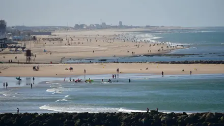 Panorámica del litoral de Cádiz tomada desde la playa de Santa María del Mar: en primer plano el espigón y, al fondo, la línea costera hasta Santibáñez, bajo un cielo despejado con fuerte viento de Levante.
