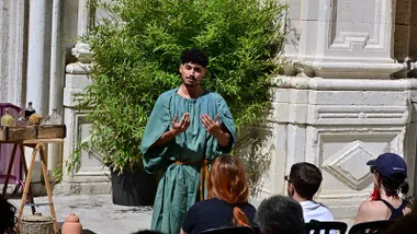 Una persona vestido a la usanza romana muestra prácticas médicas antiguas con hierbas y utensilios, durante una escenificación en el patio de la Casa del Obispo