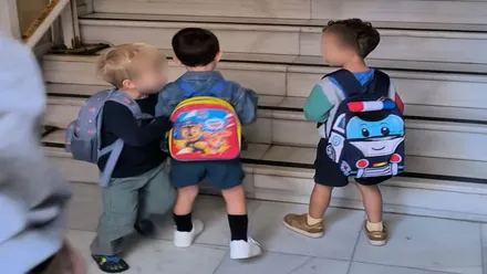 Tres niños con sus mochilas entrando en el colegio.