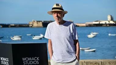 El director Fernando Trueba posa en solitario frente al photocall de La Caleta, con el mar de fondo, durante la presentación de su docuserie musical Bajañí.