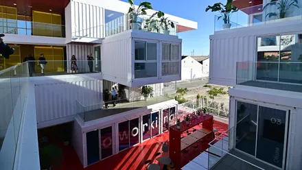 Imagen panorámica del complejo Incubazul, formado por contenedores marítimos reciclados apilados en varios niveles. Se aprecian sus terrazas abiertas, la fachada modular y el entorno urbano de la Zona Franca de Cádiz, con visitantes recorriendo el acceso principal.