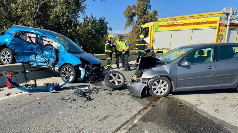 Un coche con graves daños subido sobre el quitamiedos de la A-384, junto al vehículo con el que colisionó. Al fondo, un camión de Bomberos y agentes de la Guardia Civil intervienen durante el operativo.