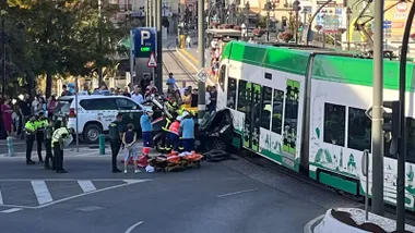 Imagen de un coche que ha chocado contra el laterald e un tranvia mientras actúan los equipos de emergencia.