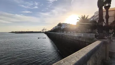 Vista de la bahía de Cádiz en una mañana despejada, con el sol brillando detrás de un edificio y las grúas del muelle recortadas en el horizonte, tomadas desde la Alameda.