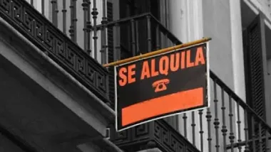 Cartel de alquiler en una terraza de una vivienda, en letras naranjas y fondo negro.