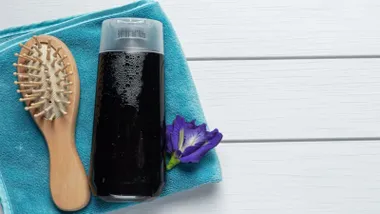 Champú anticaspa en negro junto a un cepillo y sobre una toalla color turquesa.