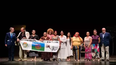 Actores en el escenario del Teatro de San Fernando portando la bandera romaní.