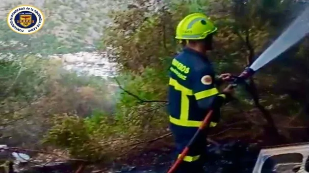 Bombero con manguera de agua sobre pastos.