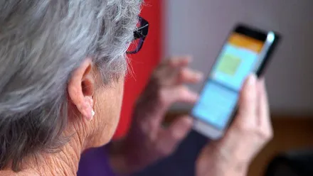 Mujer, con canas, manejando un teléfono móvil.