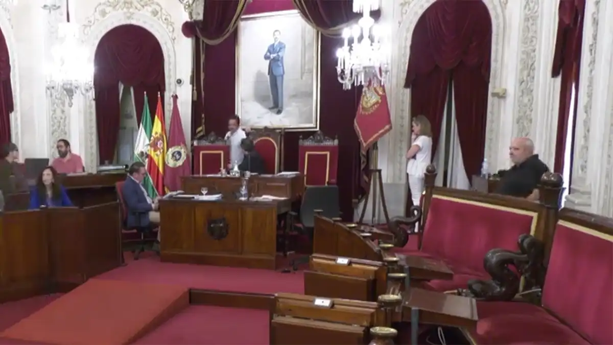 En la imagen, los lugares de PSOE y AIG vacíos y a la derecha la portavoz del PP, Mayte González Negroto, habla por teléfono con la oposición para informarles de que se puede retomar el Pleno. Mientras, el alcalde, Bruno García, habla con uno de sus asesores. Foto Onda Cádiz (YouTube).