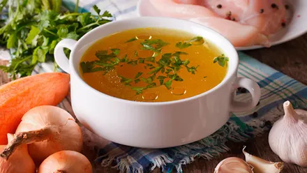 Olla de caldo de pollo con ingredientes a su alrededor.