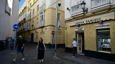 Varios peatones pasan junto a una de las cámaras de vigilancia del sistema de control de la ZBE en la Plaza de San Francisco, en pleno centro de Cádiz, frente a la Librería Raimundo.