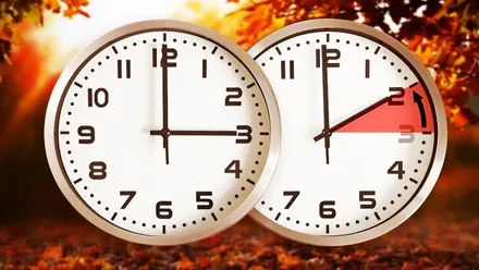 Dos relojes, uno marca las 3 y otro las 2. Fondo otoñal.