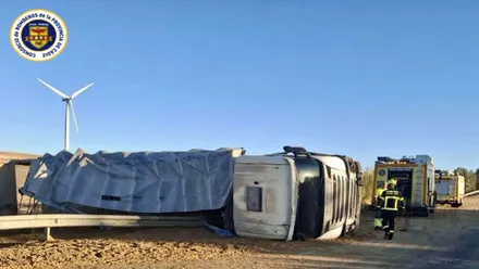Camión volcado en la carretera y bomberos asistiendo al conductor.