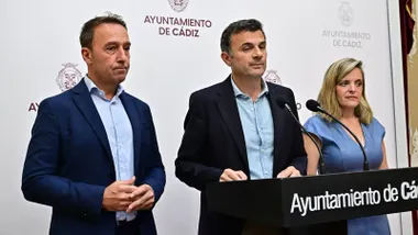 El alcalde de Cádiz, Bruno García, comparece junto a José Manuel Cossi y Mayte González ante un estrado con dos micrófonos. Detrás de ellos se distinguen el logo institucional del Ayuntamiento de Cádiz y el escudo municipal sobre un fondo blanco.