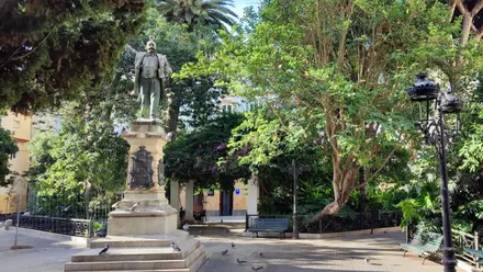 Estatua de Emilio Castelar en la Plaza de Candelaria de Cádiz, rodeada de árboles y plantas, en un día soleado de octubre.