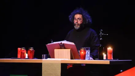 El artista gaditano Chipi La Canalla interpreta una escena de El bar nuestro de cada día durante su actuación en la Feria Internacional de Teatro y Danza de Huesca. Aparece de pie, cantando y gesticulando ante el micrófono, bajo una iluminación cálida que resalta el ambiente íntimo del espectáculo.