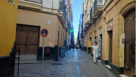 Calle de Cádiz con cielo azul despejado y una mujer caminando por ella.