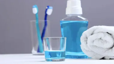 Un vaso con colutorio de color celeste, tras él un bote y vaso con cepillos de diente.