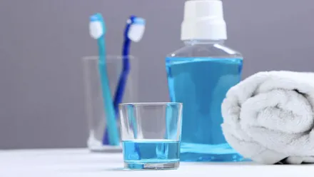 Un vaso con colutorio de color celeste, tras él un bote y vaso con cepillos de diente.