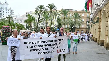 Plantilla de Ayuda a Domicilio concentradas en la Plaza de San Juan de Dios de Cádiz, sosteniendo una gran pancarta con mensajes en defensa de la municipalización y contra los impagos de la empresa concesionaria.