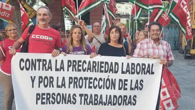 Imagen de varias personas concentradas frente a un edificio oficial en Cádiz. Llevan banderas rojas de CCOO, algunas con pancartas que reclaman “seguridad” y “dignidad laboral” para el personal de los centros de menores.