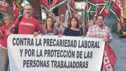 Imagen de varias personas concentradas frente a un edificio oficial en Cádiz. Llevan banderas rojas de CCOO, algunas con pancartas que reclaman “seguridad” y “dignidad laboral” para el personal de los centros de menores.