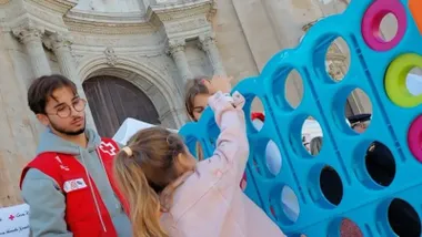 Un voluntario de Cruz Roja observa como una niña juega en una de las actividades de la organización con motivo del Día de la Banderita del año 2024 en la Plaza de la Catedral de Cádiz.