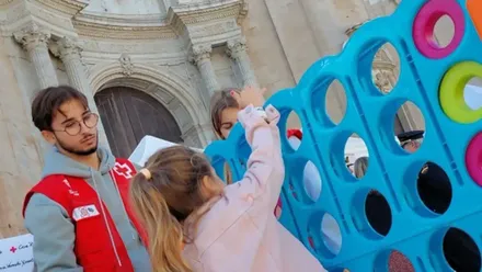 Un voluntario de Cruz Roja observa como una niña juega en una de las actividades de la organización con motivo del Día de la Banderita del año 2024 en la Plaza de la Catedral de Cádiz.