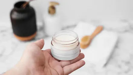 Mano sosteniendo un tarro de crema desmaquilladora.