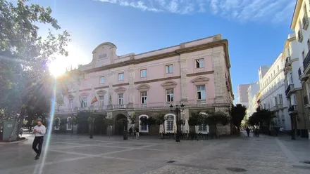 Edificio de la diputación de Cádiz en una mañana soleada visto desde la Plaza de España con un hombre con su móvil caminando hacia ella.
