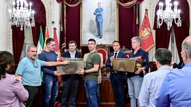 Los descendientes de dos víctimas del franquismo, Juan Diego Cortés Pacheco y Manuel Moreno Cortés, sostienen las urnas con los restos de sus familiares durante el homenaje celebrado en el Salón de Plenos del Ayuntamiento de Cádiz. Se aprecia emoción y respeto entre los asistentes.