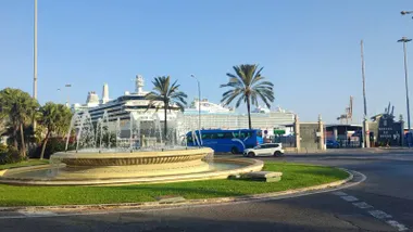 Vista de la fuente de la plaza de Sevilla en Cádiz con dos grandes cruceros atracados en el muelle bajo un cielo despejado y luminoso durante la mañana del 10 de octubre de 2025.