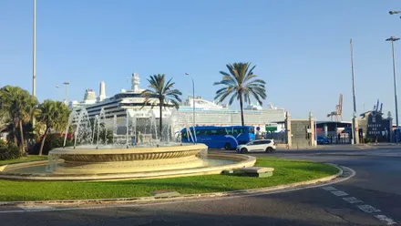 Vista de la fuente de la plaza de Sevilla en Cádiz con dos grandes cruceros atracados en el muelle bajo un cielo despejado y luminoso durante la mañana del 10 de octubre de 2025.