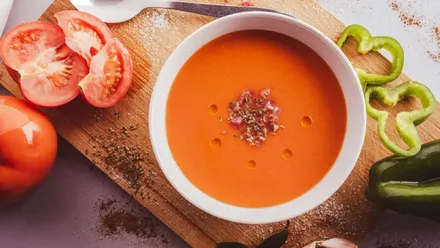 Plato de gazpacho con tomate y verduras alrededor.