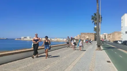 Personas caminando hacia la playa en Cádiz bajo un cielo azul despejado en un día soleado de octubre.