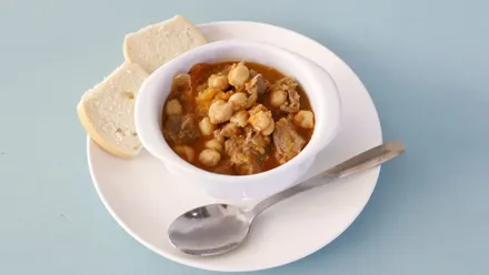 Plato con una porción de guiso, pan y una cuchara.