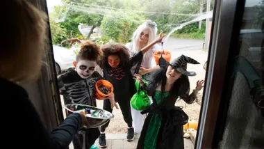 Niños y niñas disfrazados para Halloween llamando a la puerta de una casa pidiendo golosinas.