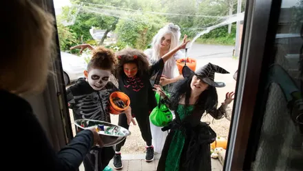 Niños y niñas disfrazados para Halloween llamando a la puerta de una casa pidiendo golosinas.